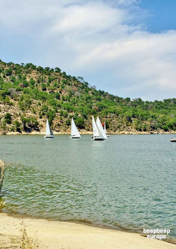 A number of small yachts are sailing on beautiful green waters, surrounded by very green, rocky hills in the background.