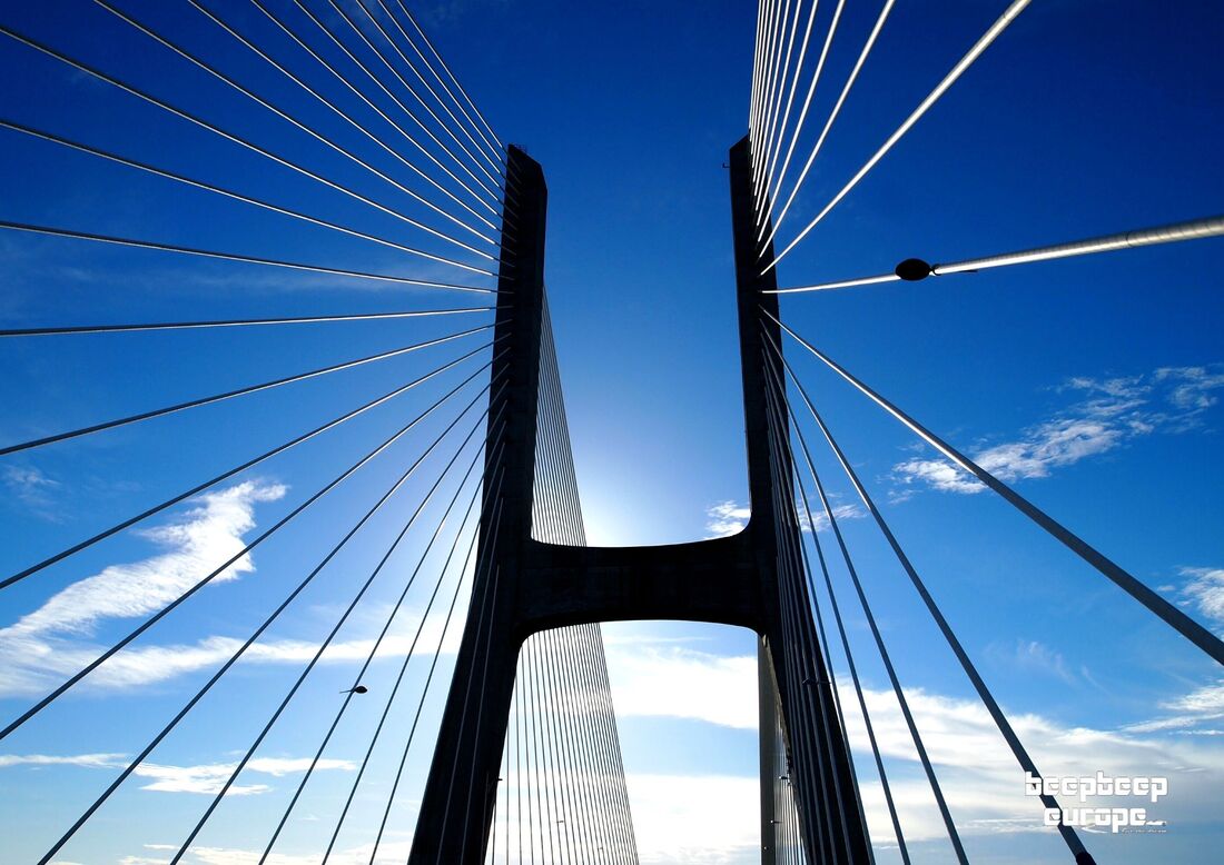 Looking up at a magnificent suspension bridge and suspension cables with vivid blue, cloudy skies in the background.